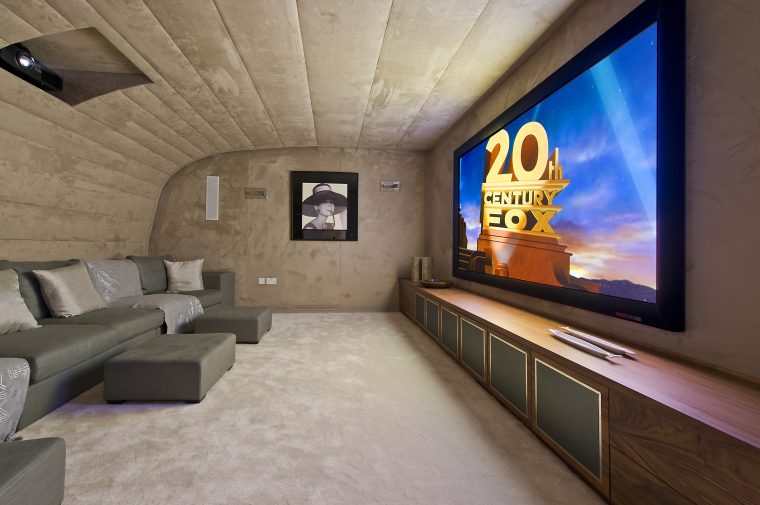 Home cinema with curved padded ceiling and built-in storage below the screen. Origins Design created the bespoke sofa seating