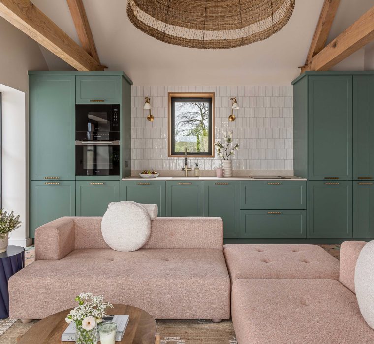 Pale pink modular sofa by bespoke furniture maker Origins Design sat in an open plan living space with a sage green kitchen